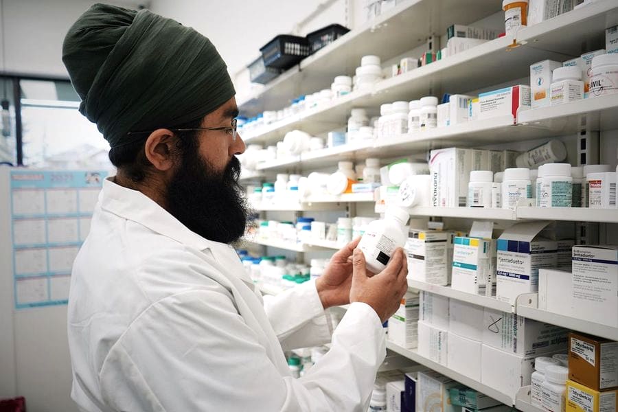 Químico farmacéutico revisando la etiqueta de un medicamento frente a las estanterías de una farmacia